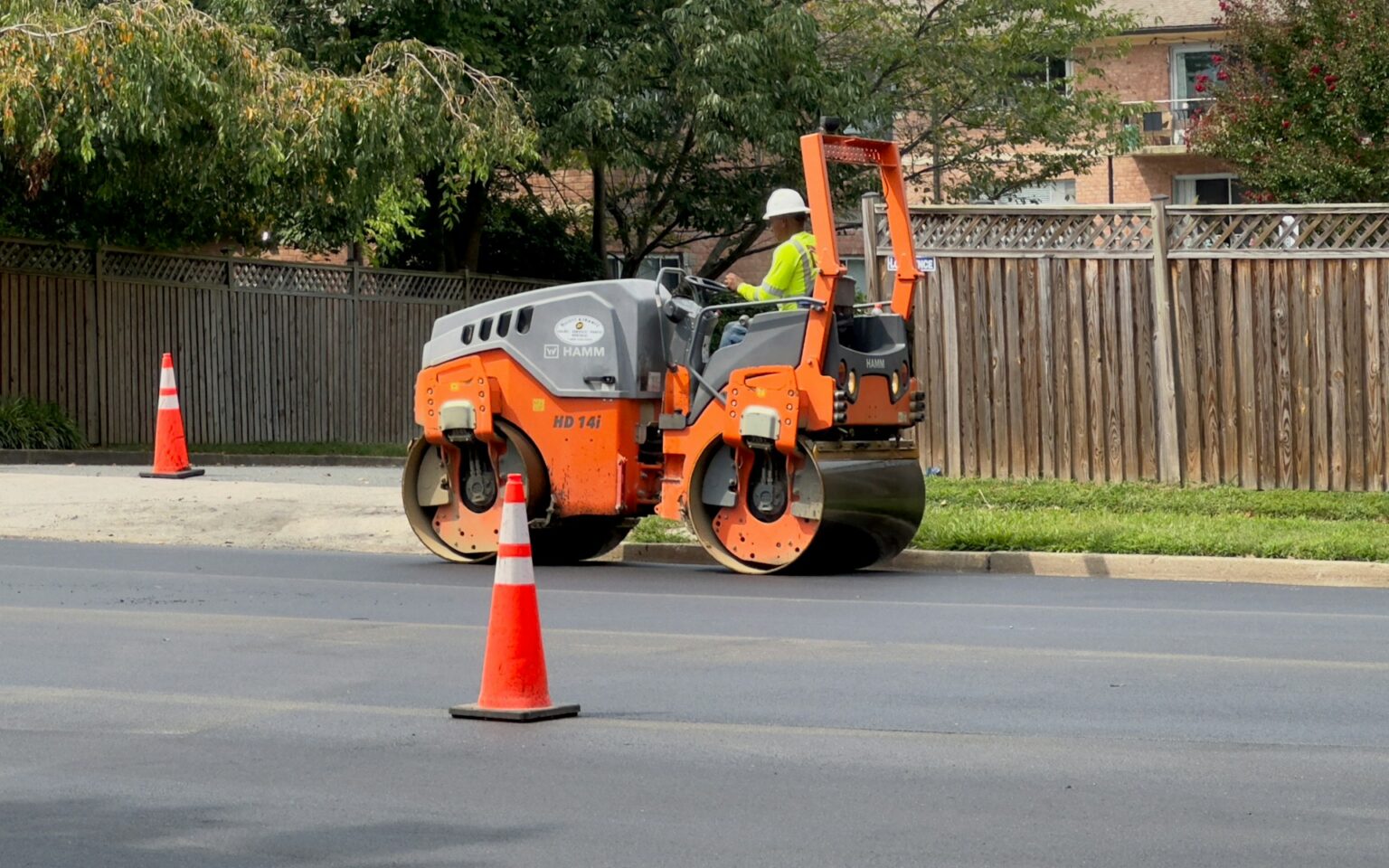 Compacteur sur une chaussée fraîchement goudronnée, derrière un cône de chantier